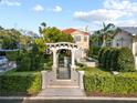 A pergola-covered gate leads to a meticulously landscaped backyard with a water feature and lush greenery at 608 Orange Ave, Clearwater, FL 33756