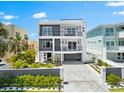Modern three-story home with gray and white exterior, balconies, manicured landscaping, and paver driveway at 32 Gulf Blvd, Indian Rocks Beach, FL 33785