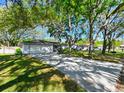 Wide view of a single-story home with a spacious driveway and a well-maintained front lawn, shaded by mature trees at 4915 Churchill Pl, Land O Lakes, FL 34639