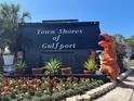Community sign for Town Shores of Gulfport with colorful flower beds and someone in a dinosaur costume at 5935 30Th S Ave # 204, Gulfport, FL 33707