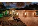 Stunning home featuring a three-car garage, brick driveway, and well-manicured landscaping at dusk at 3198 Thatcher Ln, Tarpon Springs, FL 34688