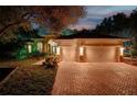 Elegant home showcasing a three-car garage, brick driveway, and lush landscaping illuminated at night at 3198 Thatcher Ln, Tarpon Springs, FL 34688
