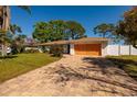 A single story home with a brick driveway and lawn with trees, bushes and a white fence at 1591 N Dakota Ne Ave, St Petersburg, FL 33703