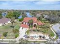 Stunning aerial view of a red-roofed home with a fountain, lush landscaping, and a picturesque lake backdrop at 4404 Lake In The Woods Dr, Spring Hill, FL 34607