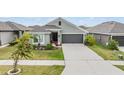 Inviting single-story home showcasing a lush lawn, gray exterior paint, and a two-car garage at 14916 Imperial Purple Ln, Wimauma, FL 33598