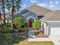 Charming single-story home with a three car garage, lush landscaping, and inviting walkway to a red front door at 12304 Silton Peace Dr, Riverview, FL 33579