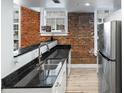 Kitchen featuring black granite countertops, stainless steel appliances, brick wall, and hardwood floors at 215 Central Ave # 4H, St Petersburg, FL 33701