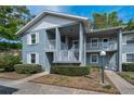 Two-story condo with a gray exterior, white railings, and a small garden area at 1438 Millstream Ln # 201, Dunedin, FL 34698