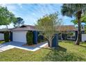 A single story blue home features a manicured lawn, shade trees, with a two car garage, and a sidewalk at 6208 Imperial Ky, Tampa, FL 33615