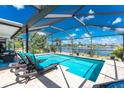 Enclosed screened lanai featuring a sparkling pool with lounge chairs and a picturesque lake view at 22322 Tennyson Ave, Port Charlotte, FL 33954