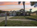 Charming single-story home with a tile roof, mature palm tree, and a well-manicured lawn at sunset at 954 Cobblestone Ln, Tarpon Springs, FL 34688