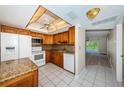 Bright kitchen featuring granite countertops, white appliances, wood cabinets, and tile floors at 938 Virginia St # 308, Dunedin, FL 34698