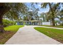 Exterior shot showcasing a blue single-story house with a long driveway, carport, and mature trees at 133 15Th Nw St, Largo, FL 33770