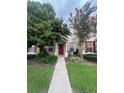 Charming home with a red front door, manicured lawn, complemented by mature trees and vibrant flowers at 30132 Wellesley Way, Wesley Chapel, FL 33543