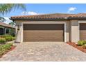 Close-up of a two-car garage with a brick paved driveway and manicured landscaping at 12379 Amica Loop, Venice, FL 34293