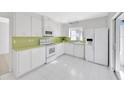 Bright kitchen featuring white cabinets, appliances, and tile floors with a glass door to outside at 13850 Sunset Dr, Largo, FL 33774