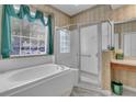 Bright bathroom featuring a soaking tub, walk-in shower, decorative wallpaper, and a large window at 19106 Abercorn Pl, Lutz, FL 33558