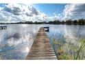Wooden dock stretching into a serene lake, reflecting the cloudy blue sky and surrounding trees at 3207 Lake Padgett Dr, Land O Lakes, FL 34639