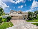 Attractive home showcasing a three-car garage, lush landscaping, and a brick-paved driveway at 8578 Gibbons Grove Loop, Land O Lakes, FL 34637