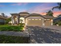 Beautiful sunset view of a one-story home featuring a manicured lawn, mature landscaping, and a three-car garage at 9905 Woodbay Dr, Tampa, FL 33626