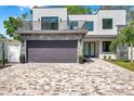 Modern two-story home featuring a balcony, stone accents, a gray garage door, and a patterned brick driveway at 2140 Catalina Dr, Clearwater, FL 33764
