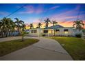 Charming single-story home featuring lush landscaping and a curved driveway, bathed in the warm hues of a vibrant sunset sky at 728 Pruitt Dr, Madeira Beach, FL 33708