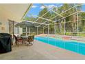 Enclosed pool area with a screened-in lanai, a dining set, and mature trees at 15014 Arbor Hollow Dr, Odessa, FL 33556