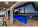 Stunning outdoor pool with illuminated water, waterfront views, and a covered patio with beautiful tile flooring at 9807 Bay Island Dr, Tampa, FL 33615