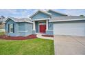 Blue single-story home with red door, lush lawn, landscaping and an attached two-car garage at 12037 Conway St, Spring Hill, FL 34609
