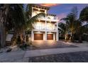 Beautiful three-story coastal home with a brick driveway, lush landscaping, and a two-car garage at 311 Spring Ave, Anna Maria, FL 34216