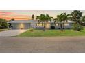 Charming single-story home with a three-car garage, lush lawn, and tropical palm tree landscaping at dusk at 636 Tarawitt Dr, Longboat Key, FL 34228