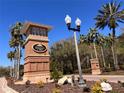 Community entrance featuring a decorative welcome sign, brick accents, and lush landscaping with palm trees at 5051 Gevalia Dr, Brooksville, FL 34604