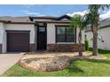 Front yard of home featuring a brick-paved driveway, rock garden, palm trees, and well-kept lawn at 10008 Celtic Ash Dr, Ruskin, FL 33573