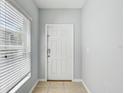 Bright entryway featuring a white front door, window with blinds, and neutral tile flooring at 10524 White Peacock Pl, Riverview, FL 33578