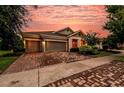 Charming single-story home with a brick driveway and manicured landscaping under a beautiful sunset sky at 6313 Brevada Ln, Apollo Beach, FL 33572