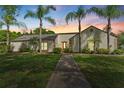 Sunset view of charming single-story home with a well-manicured lawn and mature palm trees lining the walkway at 1591 Chestnut W Ct, Palm Harbor, FL 34683