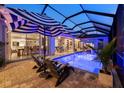 Screened-in pool area featuring blue underwater lights, striped umbrellas, lounge chairs, and outdoor dining at 8580 Ivy Stark Blvd, Wesley Chapel, FL 33545