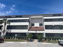 Three story condo building with lush green landscaping with a red awning, palm trees, parking spaces, and blue skies at 2583 Countryside Blvd # 3102, Clearwater, FL 33761