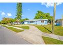 Single-story light blue home featuring a well-maintained lawn and mature trees on a sunny day at 1431 Kings Hwy, Clearwater, FL 33755
