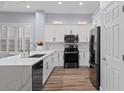 Bright kitchen featuring white cabinets, sleek black appliances, quartz countertops, and wood-look flooring at 14521 Mirasol Manor Ct, Tampa, FL 33626