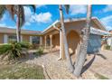 Charming home exterior featuring arched doorway, tropical landscaping, a patterned brick drive, and a blue garage at 1012 Spindle Palm Way, Apollo Beach, FL 33572