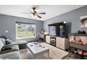 Cozy living room with a large window, ceiling fan, hardwood floors, and a comfortable gray sofa at 10849 Kensington Park Ave, Riverview, FL 33578