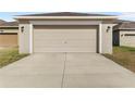 View of the neutral-colored two-car garage featuring a concrete driveway and adjacent landscaping at 13423 Lake Monroe Pl, Riverview, FL 33579