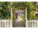 View of the purple home with white trim and fence through a flower covered archway at 522 James St, Dunedin, FL 34698