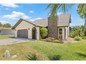 Well-maintained home with a stone chimney, lush landscaping, and an attached garage at 3626 Lake Joyce Dr, Land O Lakes, FL 34639