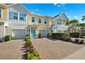 Charming multi-story townhomes featuring colorful exteriors, attached garages, and a welcoming paver driveway at 1103 Coral Ln, Dunedin, FL 34698