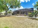 View of the home's screened-in lanai and back yard with mature trees and landscaping at 2018 E Del Webb Blvd, Sun City Center, FL 33573