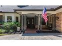 Inviting entrance with double doors, sidelights, covered porch, mature landscape, and an American flag at 213 Sheffield E Cir, Palm Harbor, FL 34683