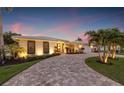 Beautiful home exterior featuring a circular driveway, lush landscaping and ambient outdoor lighting at sunset at 935 Eden Isle Ne Dr, St Petersburg, FL 33704