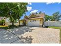 Welcoming home with an attached two-car garage, a brick-lined driveway, and a spacious front yard with mature trees at 24231 Satinwood Ct, Lutz, FL 33559